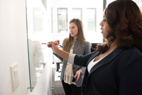 women brainstorming at whiteboard together